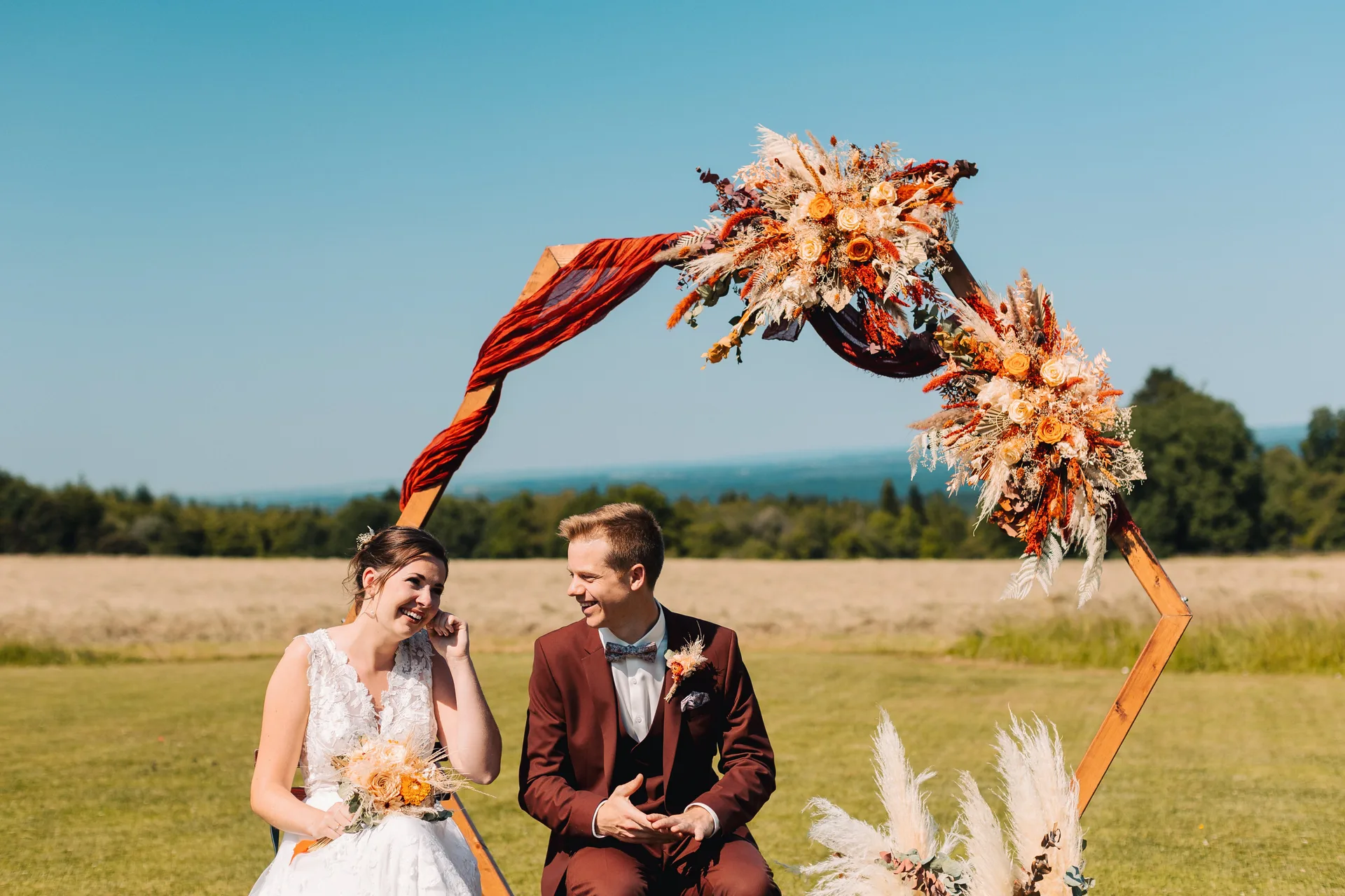 Les mariés riant sous une arche florale de pampas et fleurs séchées, Domaine de Bronromme