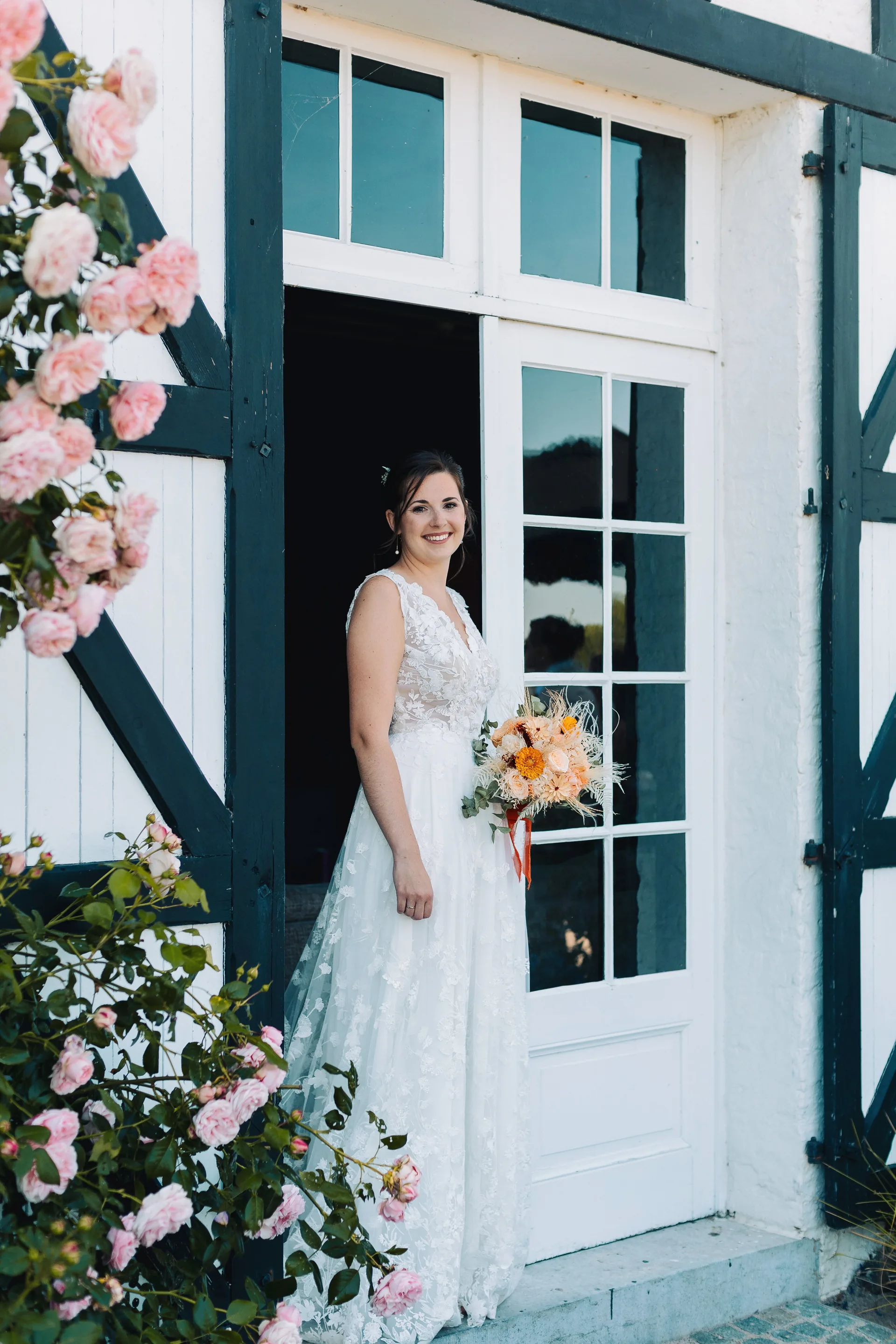 La mariée souriante dans l'encadrement d'une porte fleurie de roses